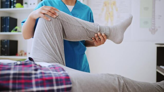 Closeup of doctor examining her patient's leg, rehabilitation clinic worker