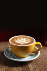 Morning coffee on a wooden table in a beautiful cup with a pattern on the foam. Aromatic coffee in a cafe.