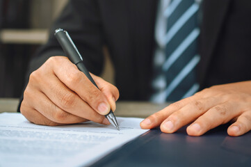 hand of businessman holding pen with writing on paper report in office