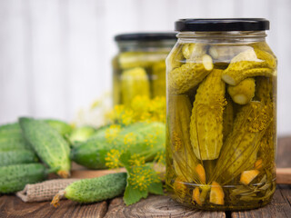 Pickled cucumbers in glass jars and fresh cucumbers and spices for making pickles on a wooden table