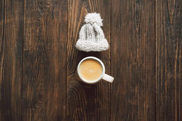 Autumn composition. Cup of coffee and autumn dried leaves, knitted little hat on wood background. Flat lay, top view