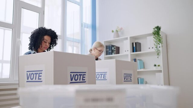 African American woman throwing voting ballot into the box at polling station