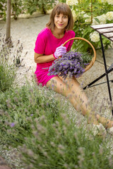 Portrait of a young cheerful woman with freshly picked lavender flowers at garden. Young housewife takes care of flowers outdoors