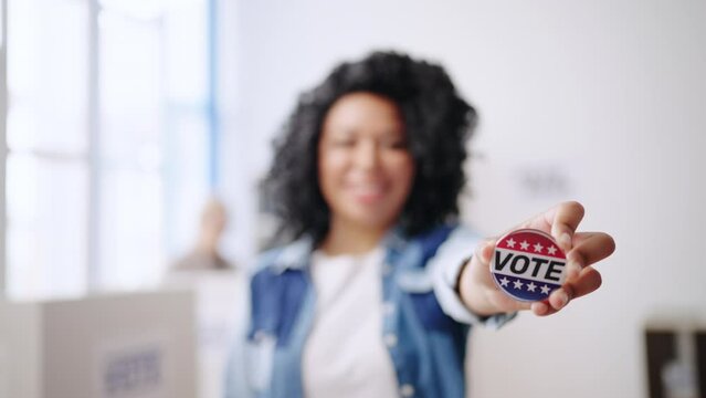 Proud woman showing her vote pin at polling station, USA voter, elections day