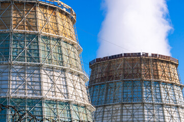 Large cooling towers of thermal power plants. White steam comes out of the cooling tower against the blue sky. Cooling tower for cooling water. A source of thermal energy in district heating systems.