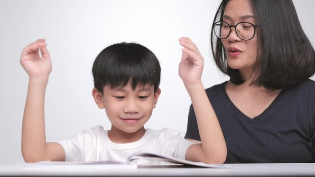 Asian mother teaches her son to read the book. A 6 year old boy learns how to spell the words.