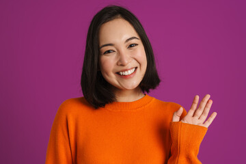 Young asian woman smiling and waving hand at camera