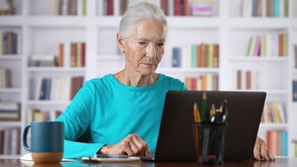 Elderly mature business woman using laptop computer sits at home office. Happy senior older employee 60s 70s businesswoman executive working typing on pc.
