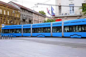long blue tram in side perspective view in Zagreb, Croatia. popular square in downtown. old classic residential buildings and stucco facades in the background. travel and tourism concept. urban scene.