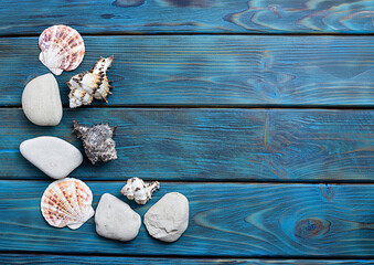 White pebbles, flat shells and sea shells on bright blue boards. Blue wooden background with orange...