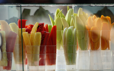 An intentionally blurry close-up of glasses with fresh-cut tropical fruit for sale at a small food court on the beach