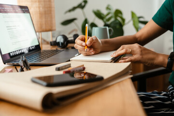 African american young woman using laptop and taking notes at home