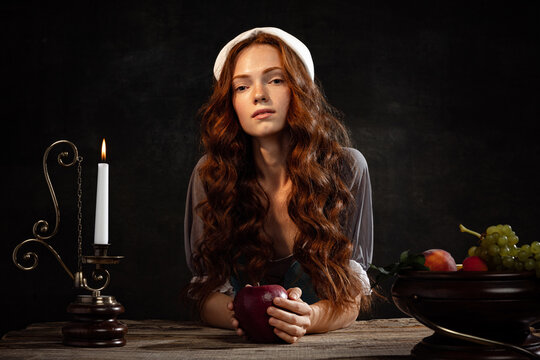Vintage portrait of young adorable redhead girl in image of medieval person in renaissance style dress isolated on dark background. Comparison of eras