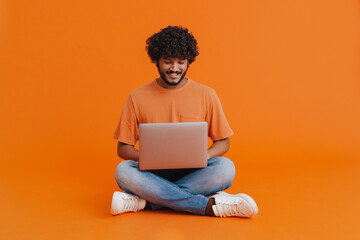 Young indian smiling man sitting with laptop in lotus pose