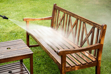 Close up view of person working cleaning pressure washing wooden garden furniture bench outdoors in...