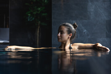 Fototapeta na wymiar Attractive young woman in a black swimsuit is relaxing in the pool.