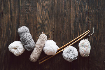 Balls of wool yarn, knitted little hat and wooden knitting needles on wooden background. Hobby craft. Concept of knitting, needlework.