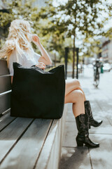 Blonde women sitting on bench at the city with black textile handbag, recycled textile handbag