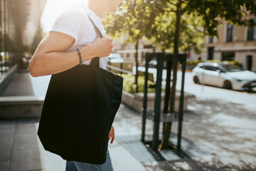 Man in white tshirt with black cotton bag in his hands. Mockup and zero waste concept