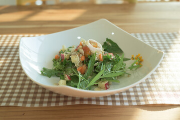 Home-made organic vegetable salad made from local vegetables and flowers in a white square-shaped dish, on a table, with copy space.