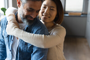 Happy diverse couple embracing and smiling with eyes closed in kitchen