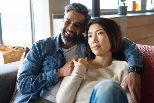 Happy diverse couple sitting on sofa in living room, embracing