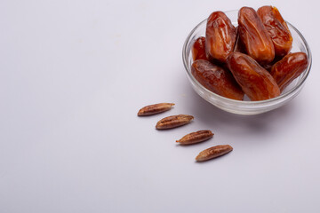 Bowl of dried dates with leaves on white background
