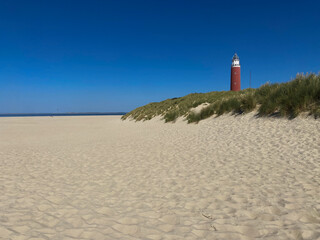 Texel lighthouse in landscape with dunes, grass and beach. On blue sky in Netherlands