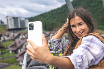 A young woman takes a selfie on a funicular in the mountains.