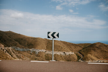 Fototapeta na wymiar Traffic signal in a curve, blue and white directional panel to slow down. In Adra, Almeria.