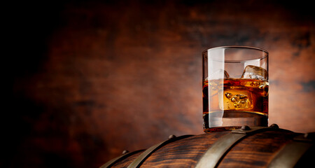 Glass of whiskey with ice cubes on the old barrel