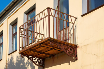 Open balcony on facade of building with forged bracket and wooden floor. Balcony with rusty iron railings in sunny day.