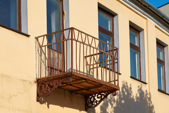 Open balcony on facade of building with forged bracket and wood floor. Balcony with rusty iron railings