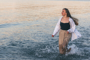 A woman walks along the sea barefoot at sunset, copy space.