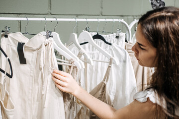 Sustainable fashion, slow fashion. Close Up Shot of female hand taking clothing rack with natural tones clothes - obrazy, fototapety, plakaty
