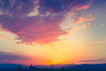 Colorful sunset sky with bright clouds and mountain range in background. Amazing natural summer evening scene.