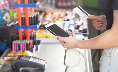 Caucasian woman using smartphone and holding credit card in supermarket.
