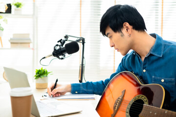 Asian young man songwriter play acoustic guitar listen song from smartphone think and write notes...