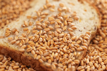 A slice of fresh bread in a pile of harvested wheat seeds. Raw grains