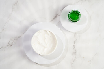 A mock-up of a round cosmetics container with cream on marble background, top view