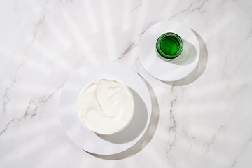 A mock-up of a round cosmetics container with cream on marble background, top view