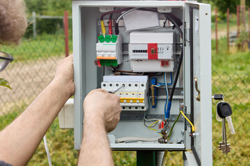 Electrician fastens connecting strip to fuse box using Phillips screwdriver.