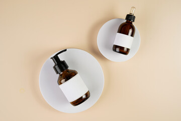 mock-up of brown cosmetics bottle with dispenser and white label, bottle with pipette on white round podium on beige colored background, top view