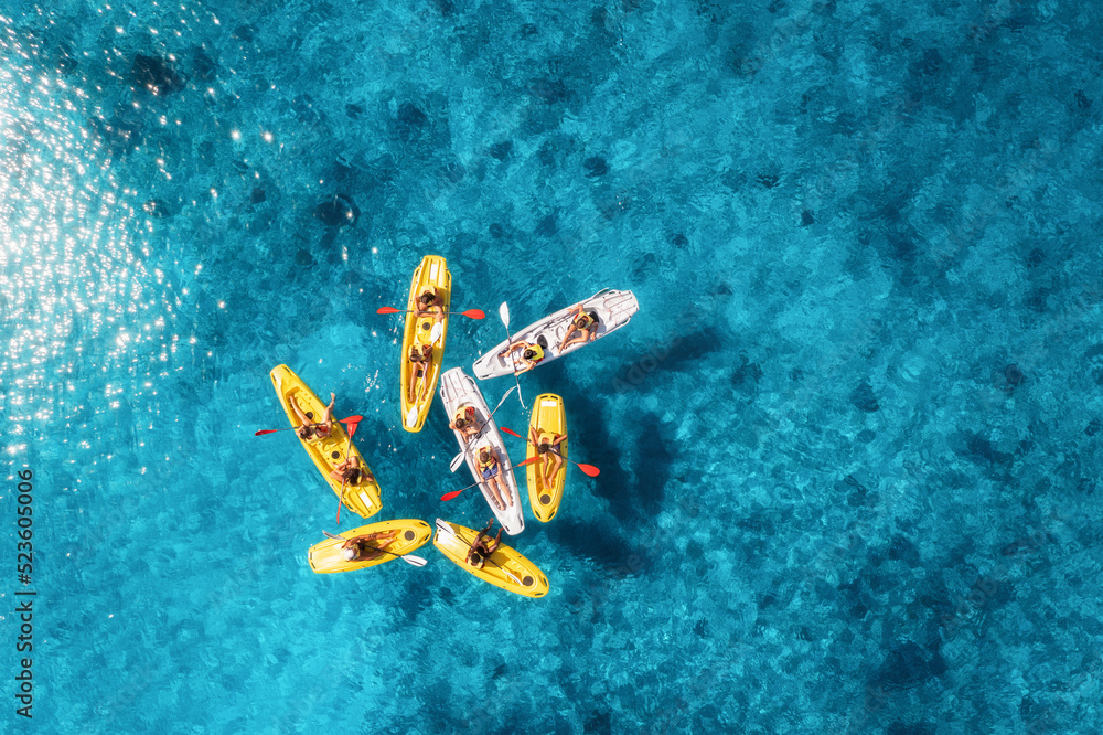 Wall mural Aerial view of yellow kayaks in blue sea at sunset in summer. People on floating canoes in clear azure water. Sardinia island, Italy. Tropical landscape. Sup boards. Active travel. Top view from drone - Wall murals