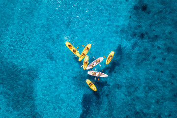 Aerial view of yellow kayaks in blue sea at sunset in summer. People on floating canoes in clear...