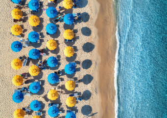 Aerial view of yellow and blue umbrellas on empty sandy beach, blue sea at sunset in summer....