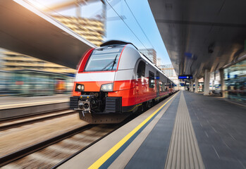 High speed train in motion on the train station at sunset in Vienna. Red modern intercity passenger train with motion blur effect. Railway platform. Railroad in Europe. Commercial transportation - obrazy, fototapety, plakaty