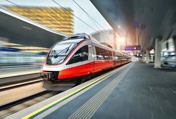 High speed train in motion on the train station at sunset in Vienna. Red modern intercity passenger train with motion blur effect. Railway platform. Railroad in Europe. Commercial transportation