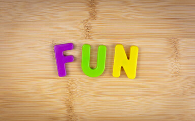 The word fun is laid out of multicolored letters on a table background with a wood texture. Concept. Game. Word. Fun.