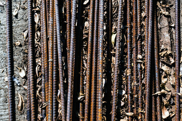Top view old rusted iron bars and dry leaves on floor. Close up to stack of straight old rusty steel reinforcement structural steel bars from construction site. Steel rod with rust. Rusty Metal Bars.